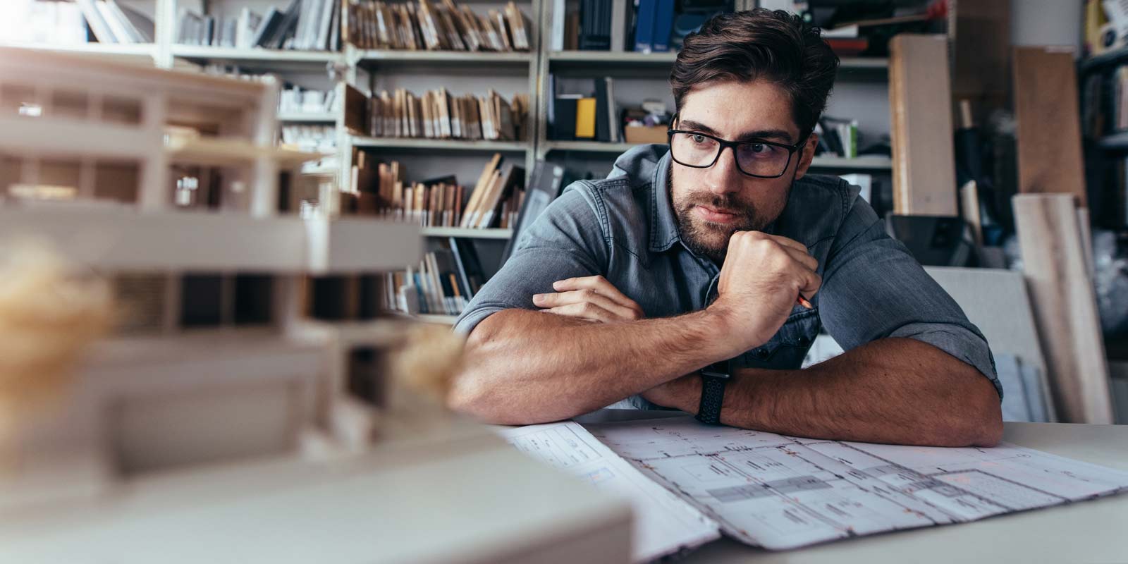 Mann betrachtet konzentriert ein Architekturmodell in einem Büro mit Bücherregalen.
